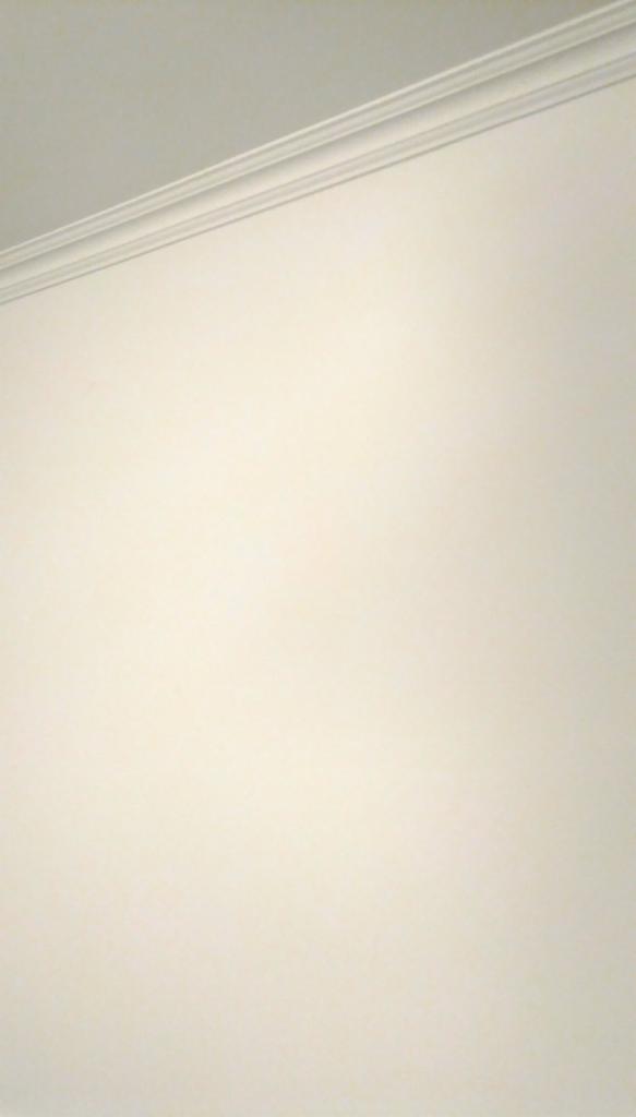Fragment białej ściany z zamontowaną listwą dekoracyjną pod sufitem, widoczne delikatne cieniowanie.