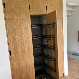 FIRMA USŁUGOWO-HANDLOWA ALINA ULMAN - Drewniana szafa na wymiar z systemem cargo, otwarte drzwi ukazują półki. Parkiet w jodełkę na podłodze. Minimalistyczny design, czarne uchwyty.