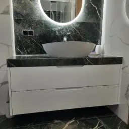 Nowoczesna łazienka z umywalką nablatową na białej szafce z dwoma szufladami, czarny blat z marmurkowym wzorem, podświetlane lustro owalne, ściany i podłoga wyłożone płytkami imitującymi marmur.