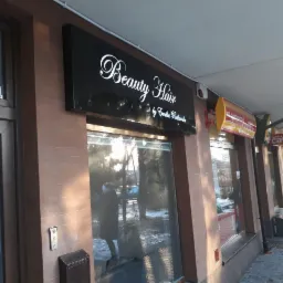 Czarny szyld reklamowy z białym napisem 'Beauty Hair by Emilia Rutkowska' nad wejściem do salonu, widoczny z zewnątrz na tle chodnika i innych lokali.