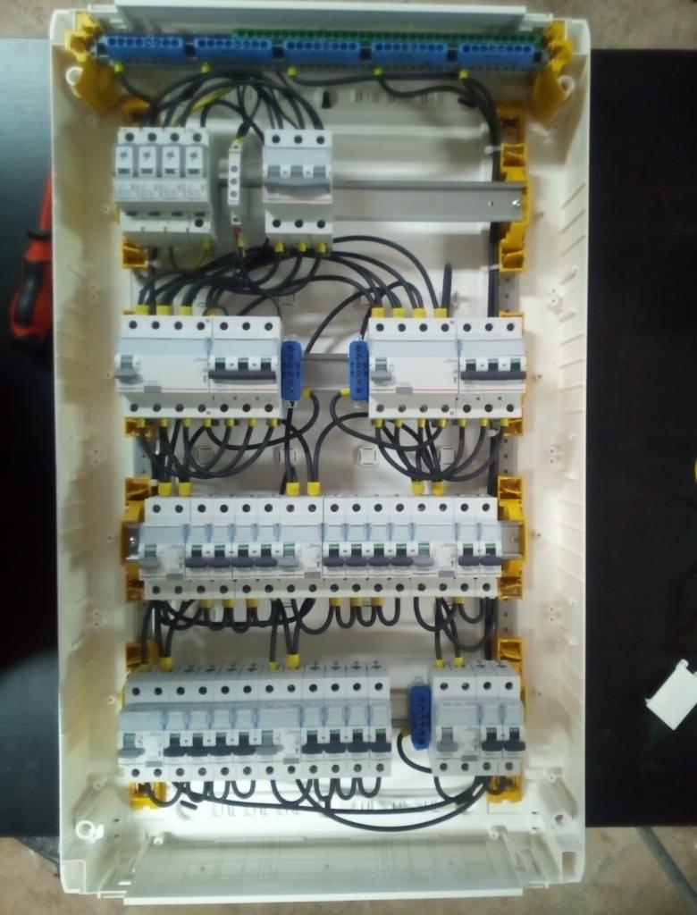 Wnętrze skrzynki rozdzielczej z zamontowanymi bezpiecznikami i okablowaniem, widok z góry na białym tle obudowy z żółtymi elementami mocującymi.