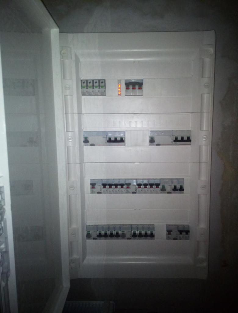 Otwarta skrzynka bezpiecznikowa z zainstalowanymi wyłącznikami różnicowoprądowymi i nadprądowymi, widoczne przewody i elementy mocujące.