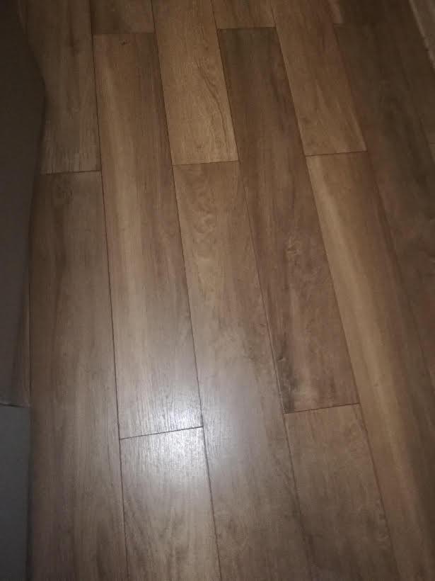 Fragment podłogi z paneli drewnopodobnych, widoczne łączenia między panelami, zarys mebla w lewym górnym rogu.