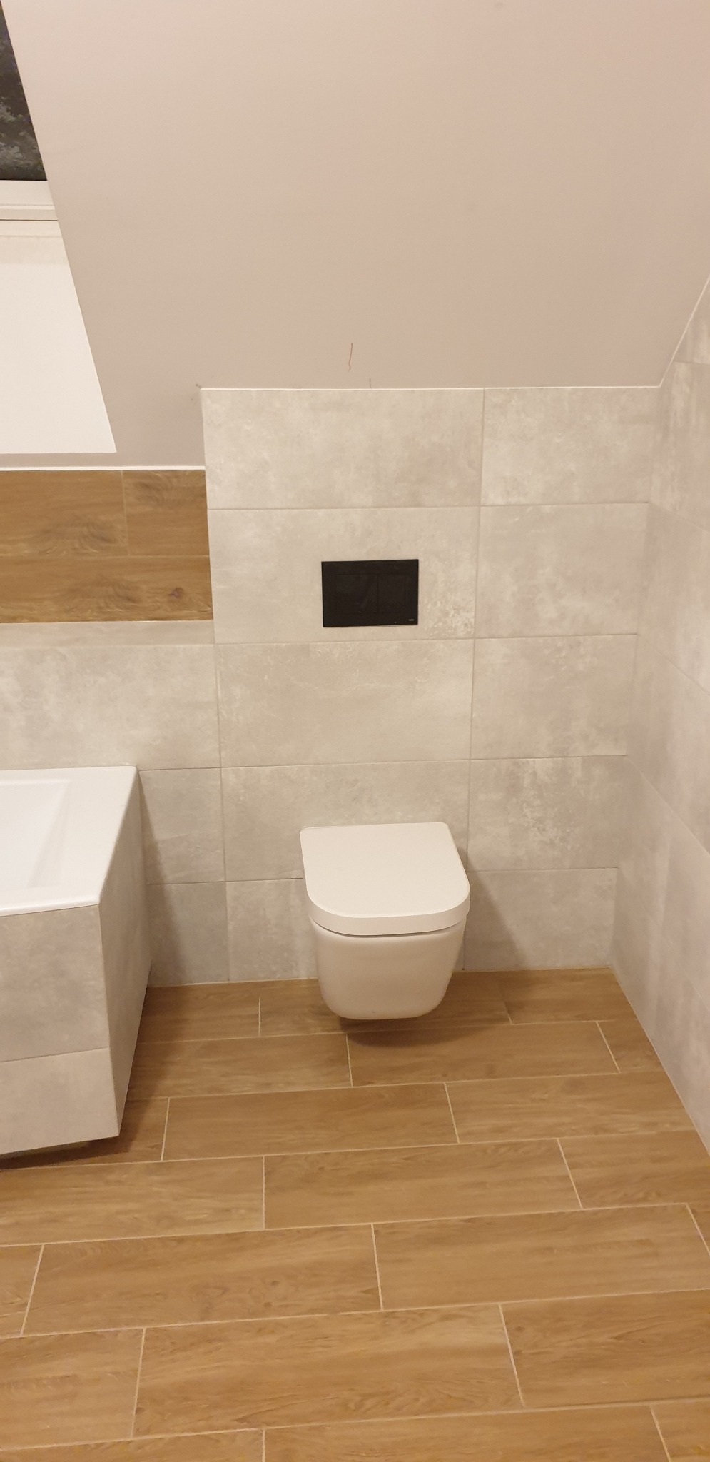 Nowoczesna łazienka w odcieniach beżu i brązu z podwieszaną toaletą i płytkami imitującymi drewno na podłodze, widok na narożnik z wanną.