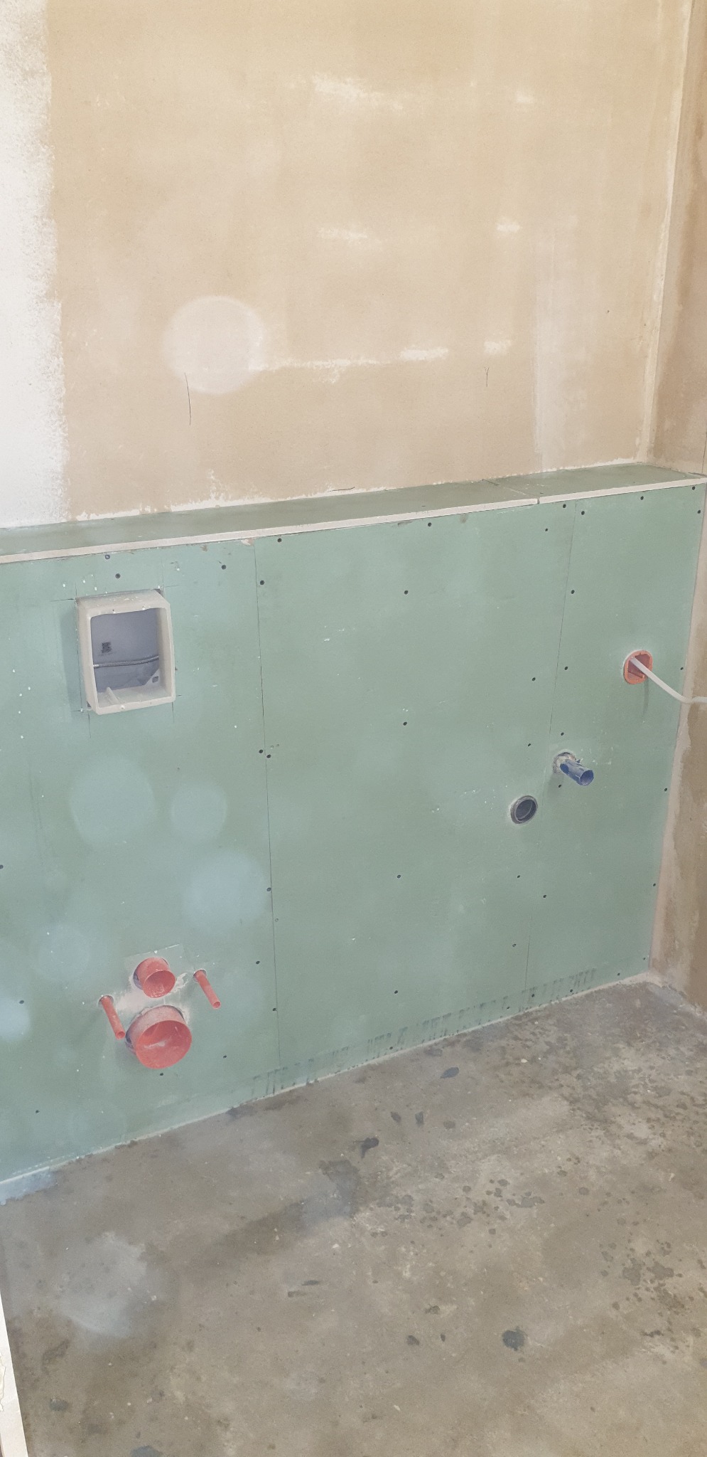 Surowa ściana w trakcie przygotowania do prac wykończeniowych w łazience w Gnieźnie, widoczne płyty gipsowo-kartonowe, otwory na instalacje wodno-kanalizacyjne i elektryczne, surowy beton na podłodze.