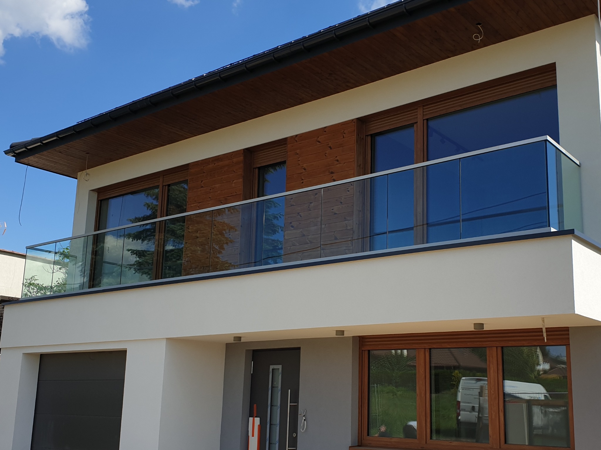 Nowoczesny dom z balkonem zabezpieczonym szkłem, widok z zewnątrz w słoneczny dzień.