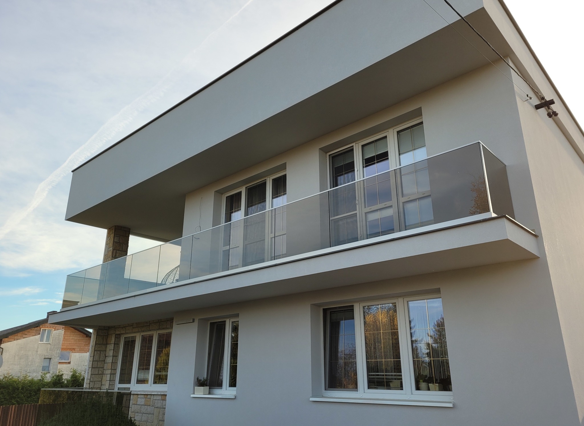 Nowoczesny balkon z przeszkloną balustradą, widok z dołu, stonowana kolorystyka budynku.