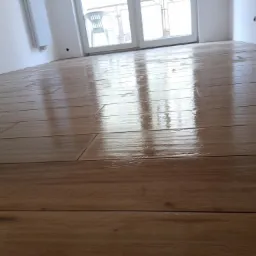 Świeżo położona, błyszcząca podłoga z paneli imitujących drewno w pustym pokoju z białymi ścianami i oknem balkonowym.