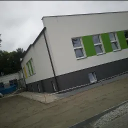 Nowo pomalowana elewacja budynku z zielonymi i żółtymi akcentami wokół okien, widoczna szara podstawa i teren w trakcie prac wykończeniowych.