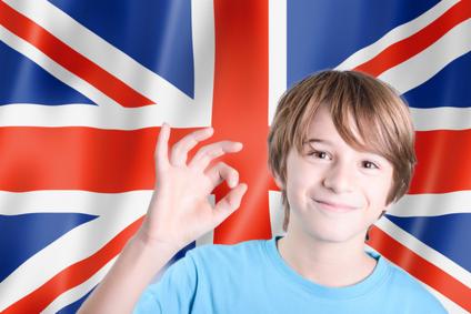 Uśmiechnięty chłopiec pokazuje znak OK na tle flagi Wielkiej Brytanii.
