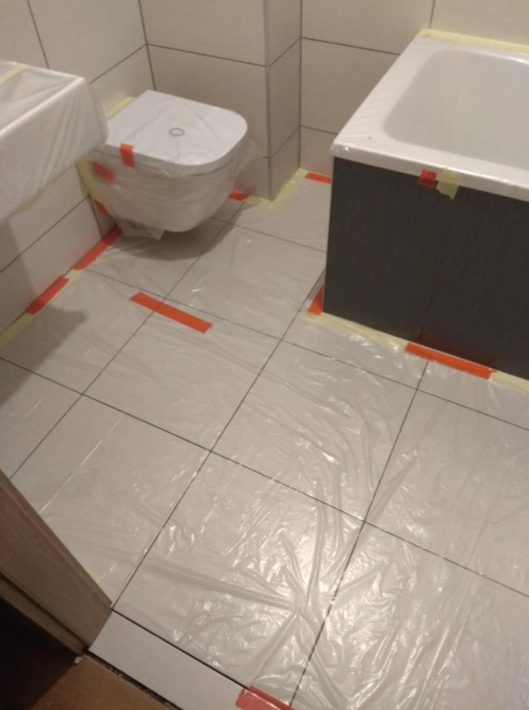 Łazienka w trakcie zabezpieczania folią i taśmą malarską przed pracami remontowymi, widoczne zakryte toaleta, umywalka i wanna.