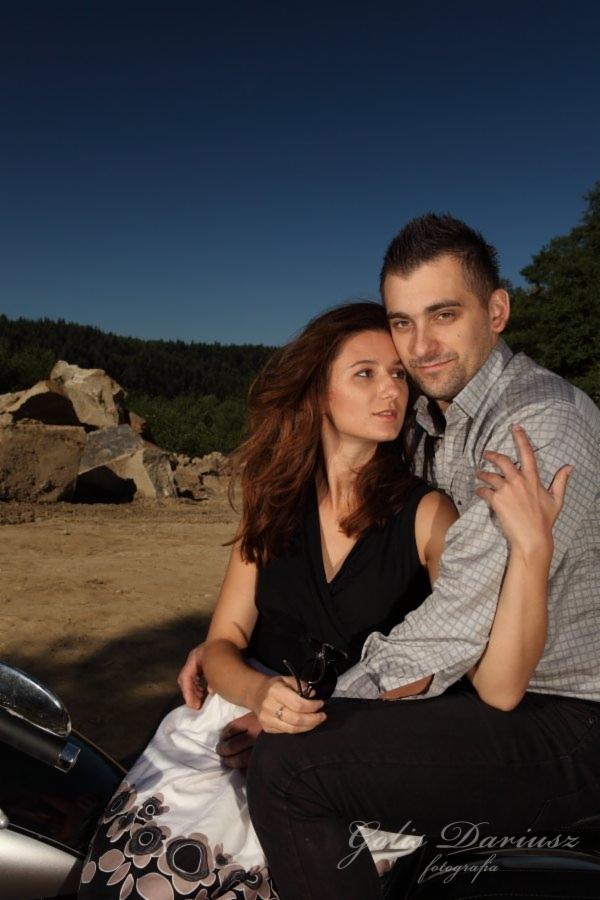 Para narzeczeńska pozuje na tle kamieniołomu, ona w czarnej bluzce i kwiecistej spódnicy, on w szarej koszuli w kratę, trzymają się blisko.