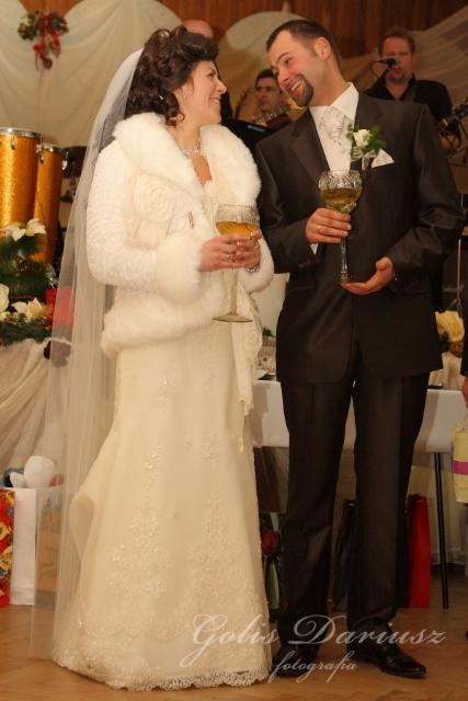 Uśmiechnięta para młoda w trakcie toastu podczas wesela, panna młoda w futrzanym okryciu, w tle zespół muzyczny.