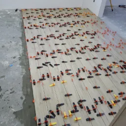 Układanie podłogi z płytek imitujących drewno, z użyciem klipsów poziomujących, widoczny fragment surowej posadzki.