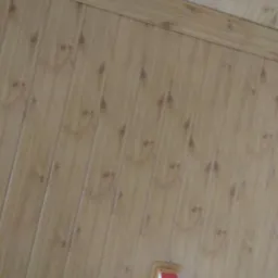 Pionowe panele ścienne z imitacją drewna, widoczne pod kątem, z fragmentem białej ściany z czerwoną listwą przypodłogową w dolnym rogu.