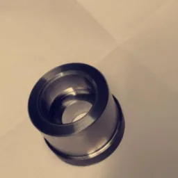 Metalowy pierścień z wewnętrznym otworem, obrobiony na tokarce, leżący na jasnym tle. Widoczne ślady obróbki skrawaniem i refleksy światła na powierzchni.