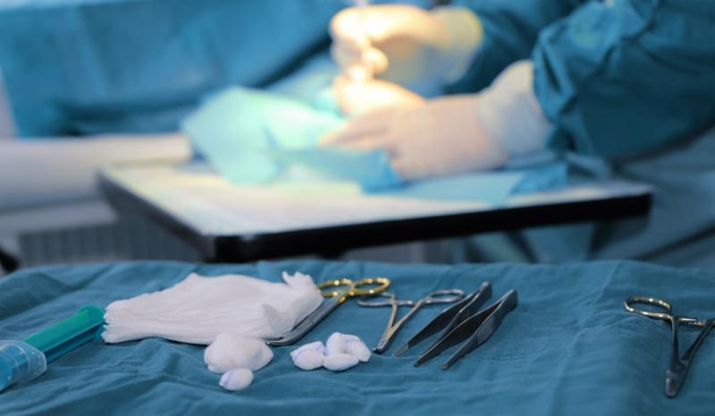 Sala operacyjna z narzędziami chirurgicznymi na stole, w tle dłonie chirurga w trakcie zabiegu.