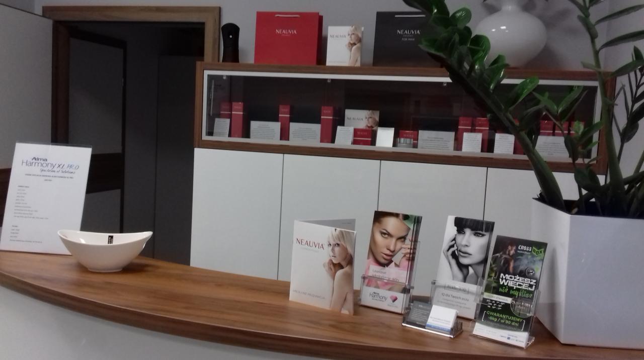 Recepcja gabinetu z produktami i ulotkami reklamowymi Neauvia oraz urządzeniem Alma Harmony XL PRO na drewnianym blacie