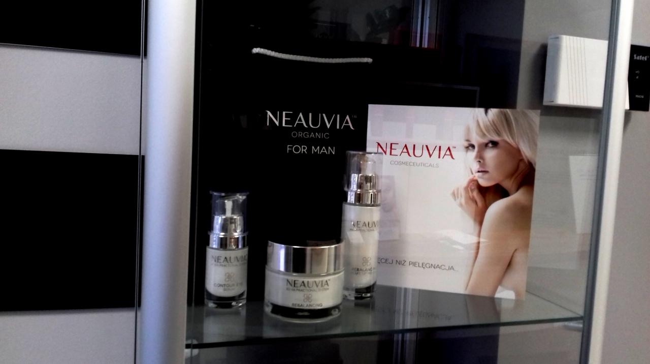 Zestaw kosmetyków marki Neauvia w szklanej witrynie, widoczna torba reklamowa z logo i plakat z wizerunkiem kobiety.