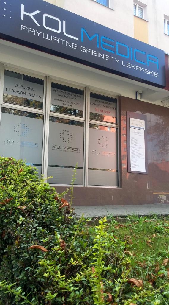 Fasada budynku z szyldem 'KOLMEDICA Prywatne Gabinety Lekarskie', okna z informacjami o usługach: chirurgia, ultrasonografia, laseroterapia, profesjonalne kosmetyki lekarskie Neauvia. Przed...