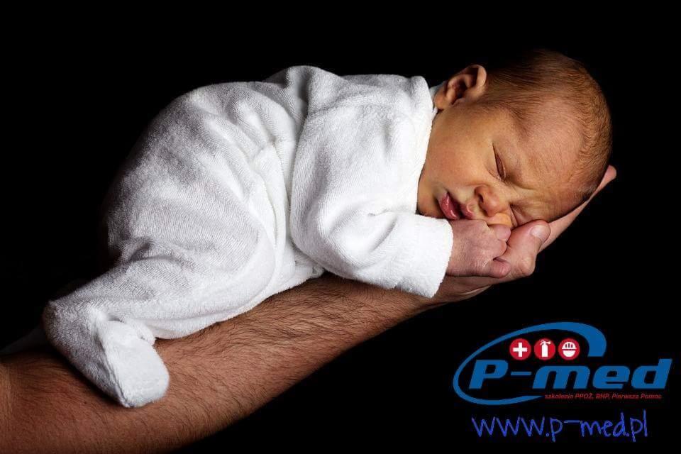Noworodek w białym ręczniku śpiący na dłoni dorosłego mężczyzny, w tle logo firmy P-med oferującej szkolenia BHP i pierwszą pomoc.
