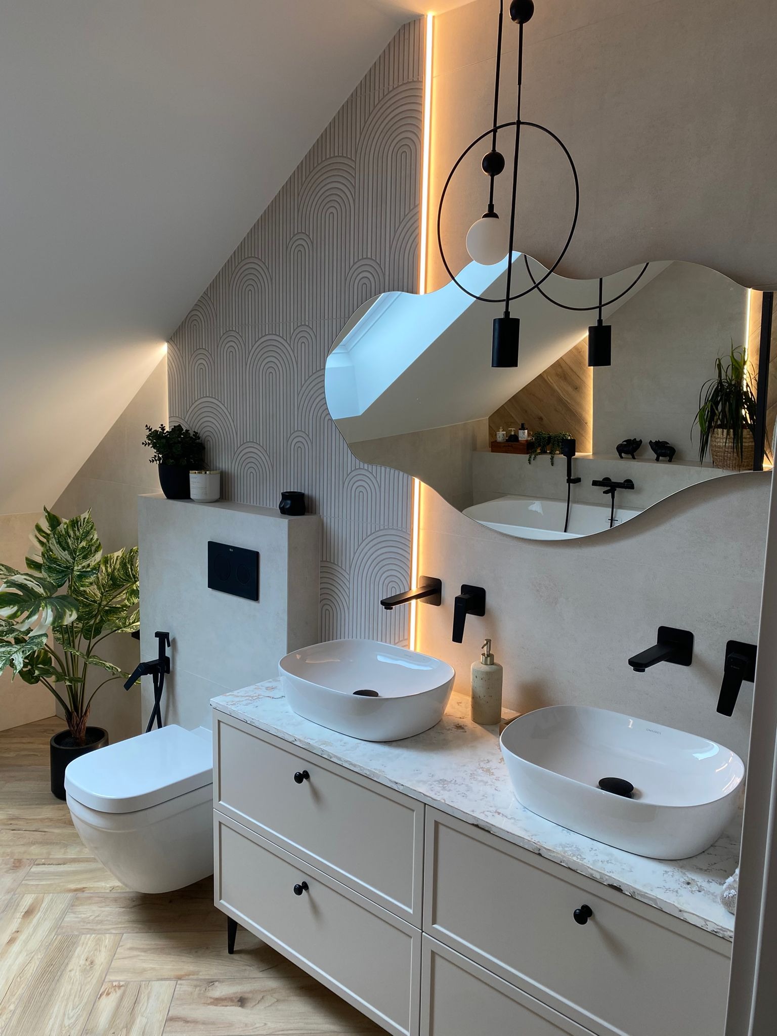 Nowoczesna łazienka na poddaszu z dwoma umywalkami nablatowymi, armaturą w czarnym macie i dekoracyjną tapetą w geometryczne wzory. Uwagę przyciąga designerska lampa.