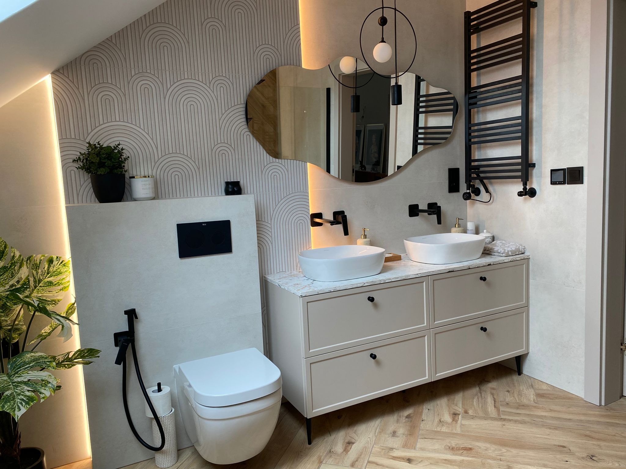 Nowoczesna łazienka na poddaszu z umywalkami nablatowymi, lustrem o nieregularnym kształcie i grzejnikiem drabinkowym. Parkiet w jodełkę, subtelne oświetlenie.