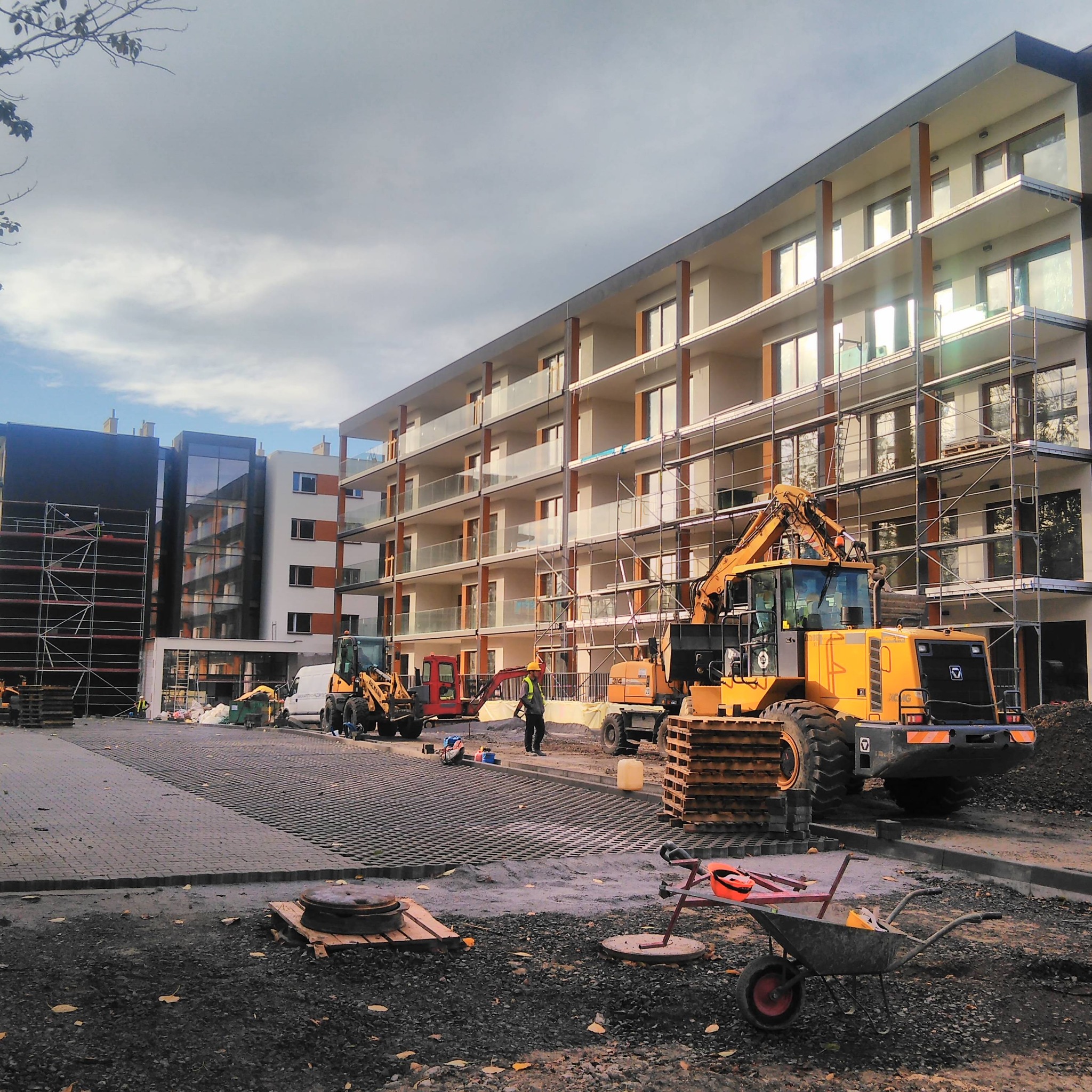 Budowa nowego budynku wielorodzinnego w Opolu, z widocznymi rusztowaniami, ciężkim sprzętem budowlanym i pracownikami w żółtych kaskach.