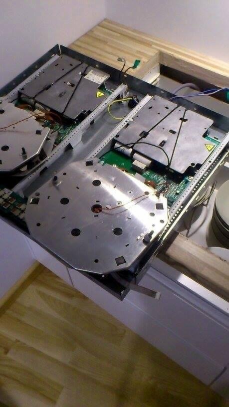 Wnętrze rozmontowanej płyty indukcyjnej z widocznymi elementami elektronicznymi i metalowymi osłonami na blacie kuchennym z jasnego drewna.