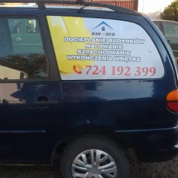 Granatowy samochód z reklamą firmy budowlanej DAW-BUD, oferującej docieplanie budynków, usługi malarskie, szpachlowanie i wykończenia, z numerem telefonu na bocznej szybie.
