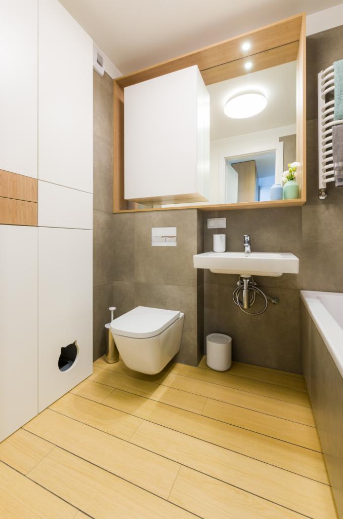 Nowoczesna łazienka z beżowymi płytkami, podwieszaną toaletą, umywalką nablatową, drewnianymi akcentami i szafką z otworem w kształcie głowy kota.