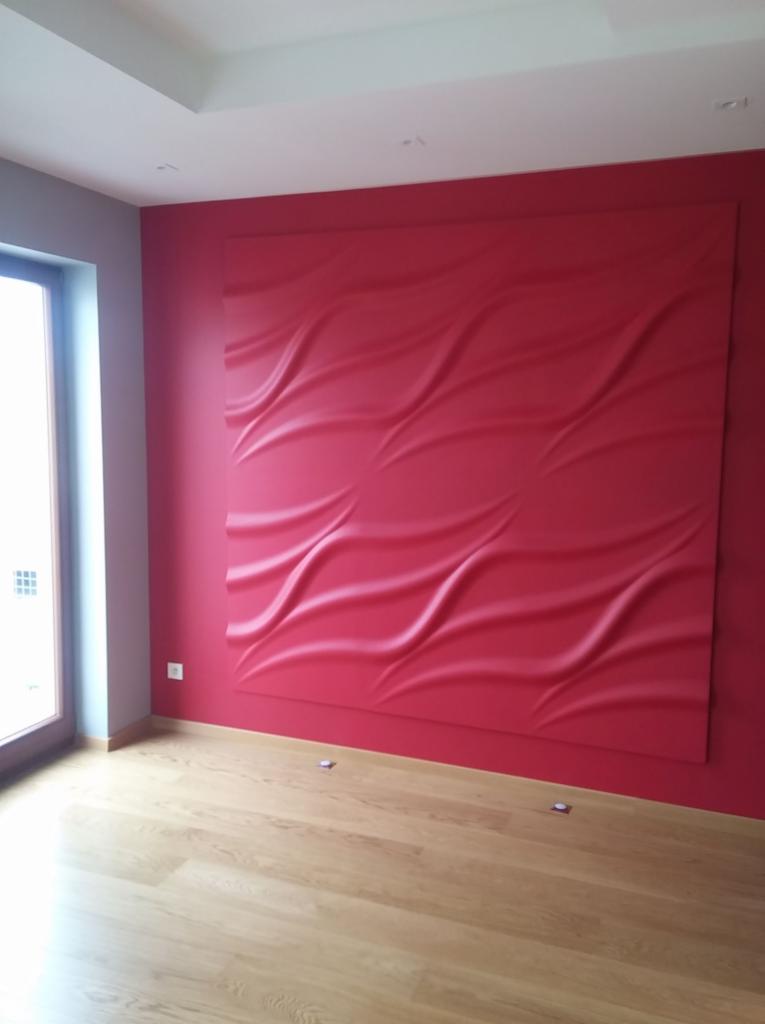 Czerwona ściana z panelami 3D o falistym wzorze, jasna drewniana podłoga, widok na okno i fragment sufitu.
