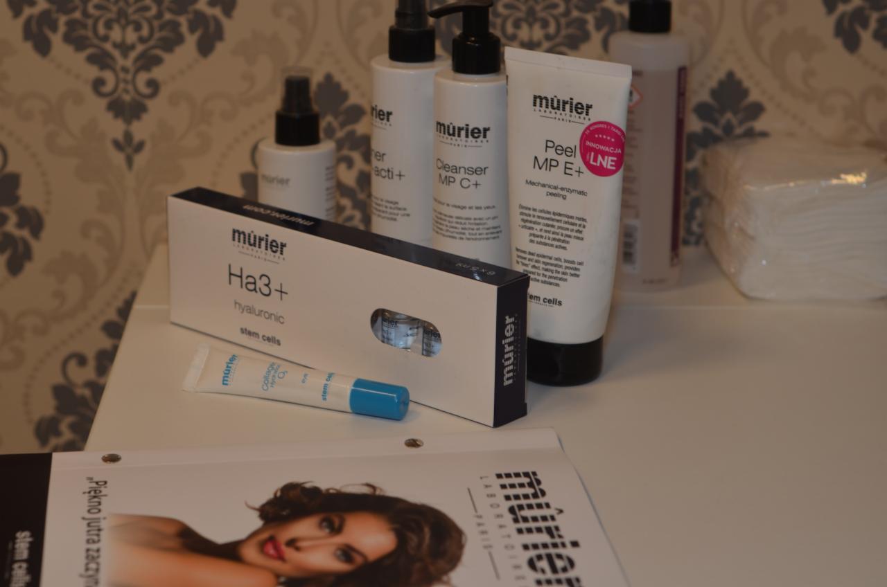 Zestaw kosmetyków marki Mürier na białym blacie: peeling enzymatyczny, cleanser, serum z kwasem hialuronowym w ampułkach, krem pod oczy i ulotka reklamowa z wizerunkiem kobiety.