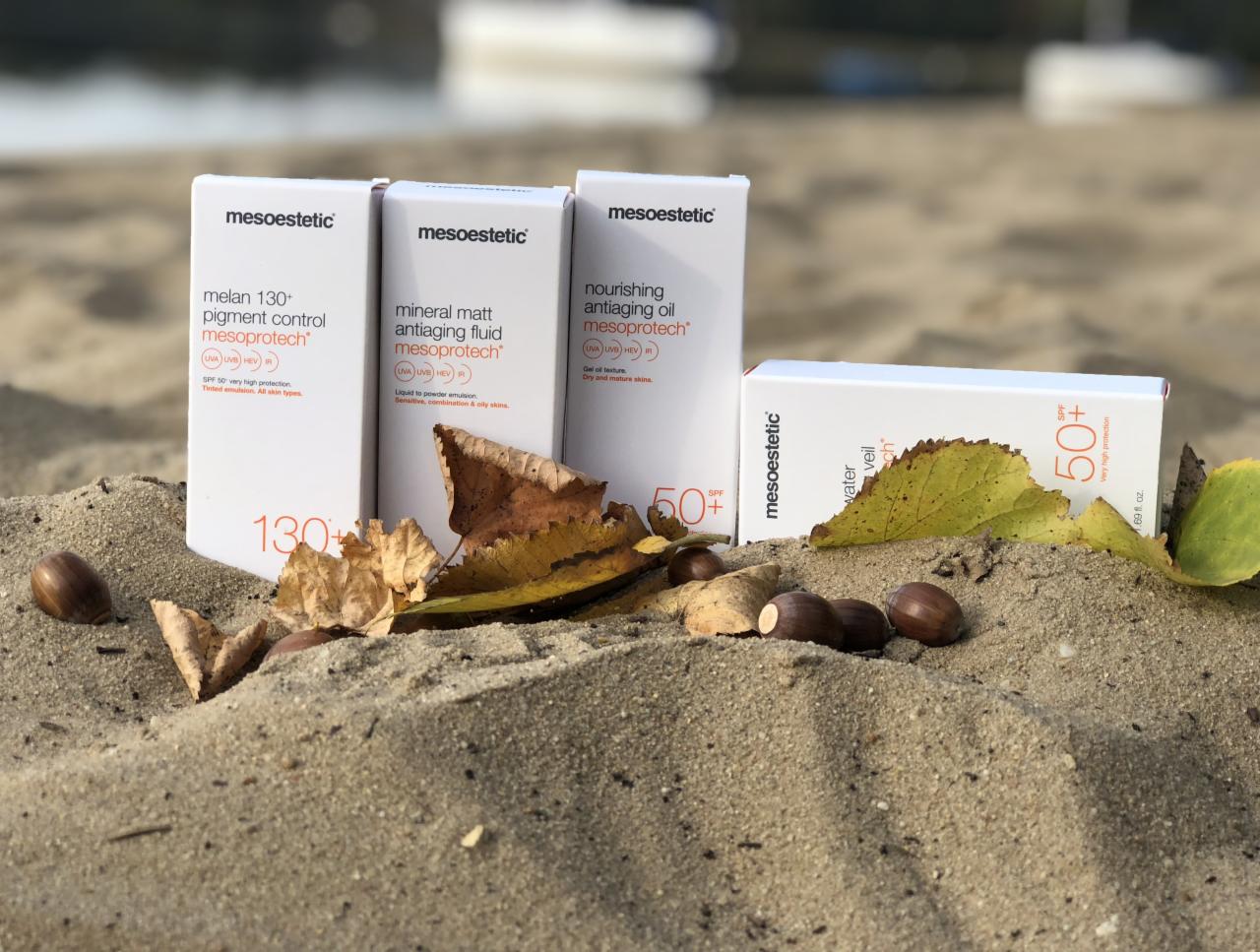 Zestaw kosmetyków Mesoestetic z filtrem SPF na piasku z liśćmi i żołędziami, prezentacja produktów do ochrony przeciwsłonecznej.