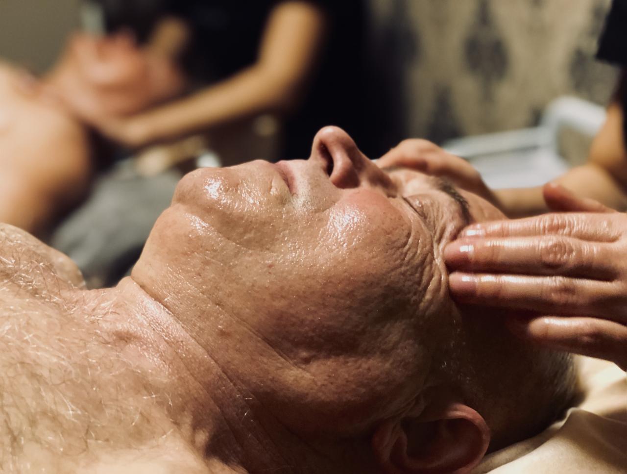 Mężczyzna leżący z zamkniętymi oczami podczas masażu twarzy, z widocznym napięciem skóry i skupieniem na okolicach oczu.