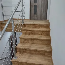 Drewniane schody z metalową balustradą w nowoczesnym wnętrzu, widok z dołu na górę, drzwi w tle.