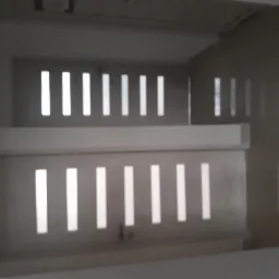 Dwa rzędy białych, pionowych przesłon w ścianie, tworzące efekt świetlny na szarej ścianie. Widoczne niedoskonałości w wykończeniu.