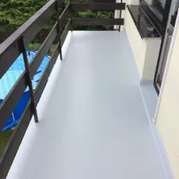 Gładka, szara powierzchnia balkonu z drewnianą balustradą; w tle widoczny basen ogrodowy i zieleń.