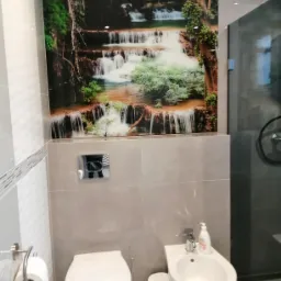 Nowoczesna łazienka z białą armaturą, szarymi płytkami i dekoracyjnym panelem ściennym z motywem wodospadu.