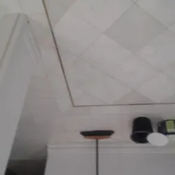 Przygotowania do prac malarskich: widok z góry na podłogę z kwadratowych płytek, białą listwę przypodłogową, wiadro z farbą, pędzel i inne akcesoria malarskie.