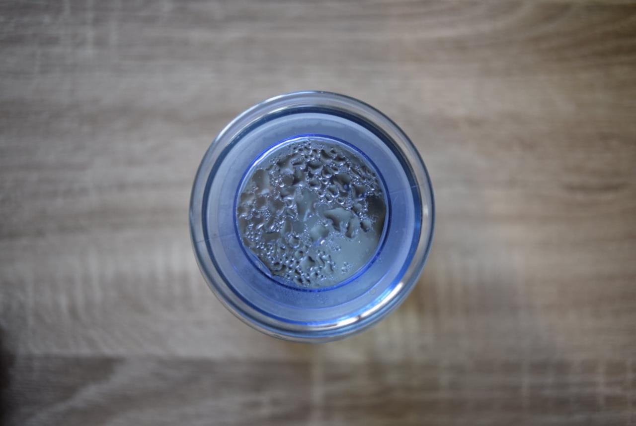 Szklanka z wodą i kroplami pary na wewnętrznej ściance, widziana z góry na drewnianym blacie.