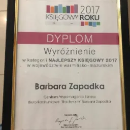 Dyplom z wyróżnieniem dla Barbary Zapadki jako Najlepszego Księgowego 2017 w województwie warmińsko-mazurskim, wręczony przez Dziennik Gazeta Prawna, oprawiony w czarną ramę ze złotym obramowaniem.