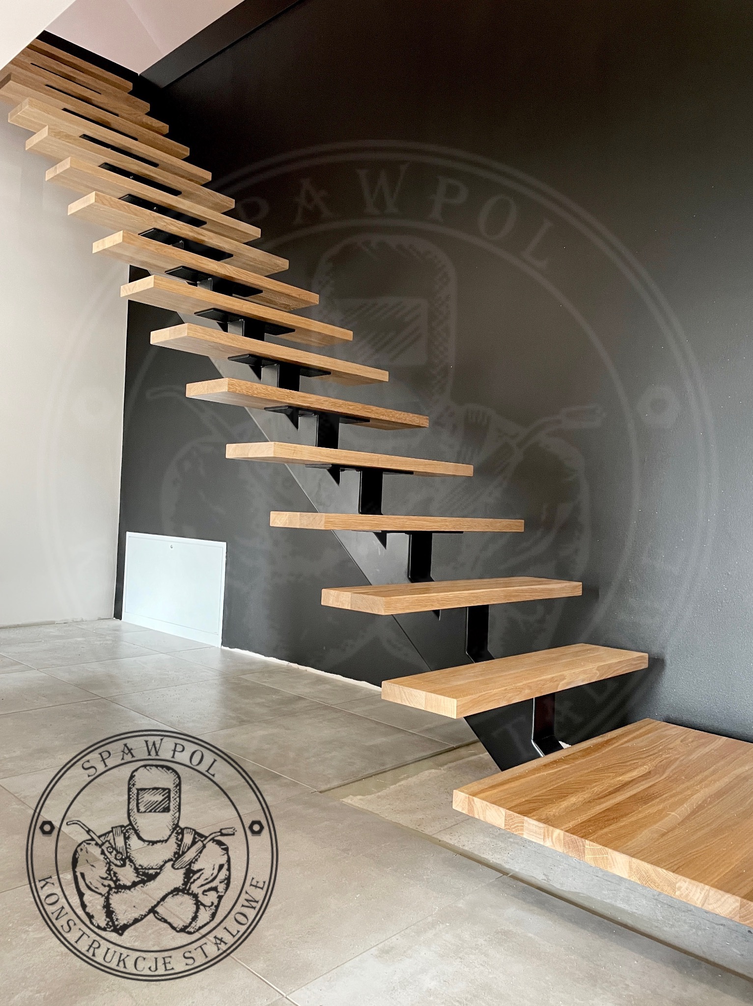 Ażurowe schody z drewnianymi stopniami i czarną, metalową konstrukcją w Szczawnie-Zdroju. Nowoczesny design z logo firmy na ścianie w tle.