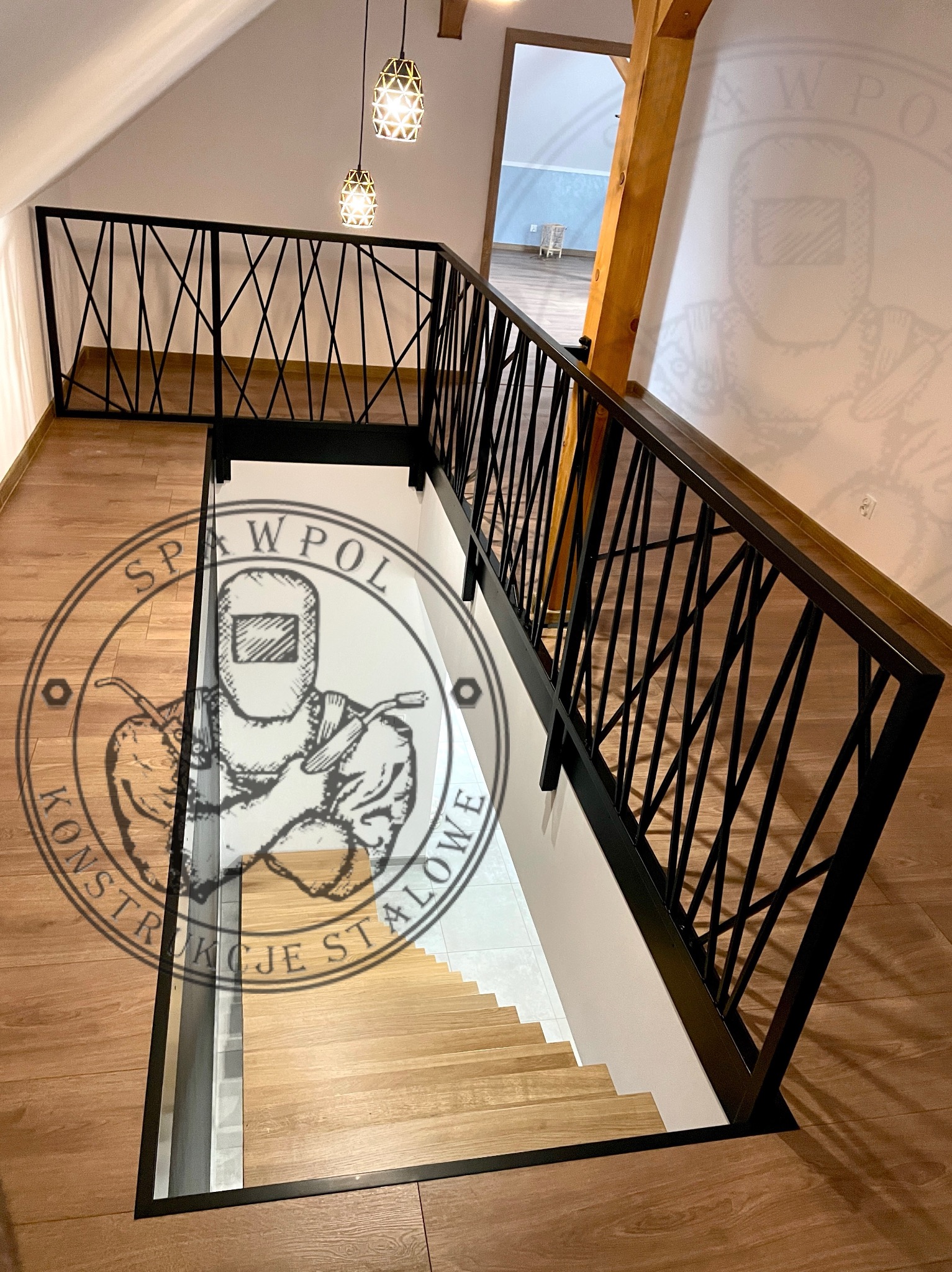 Nowoczesna balustrada metalowa w kolorze czarnym, z geometrycznym wzorem krzyżujących się prętów, zamontowana przy drewnianych schodach w jasnym wnętrzu.