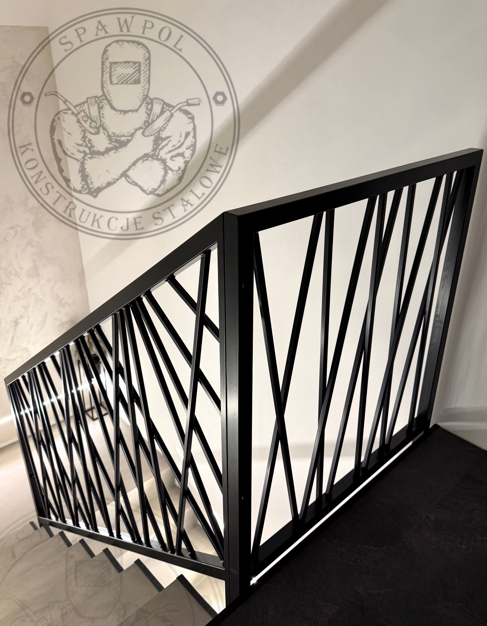 Nowoczesna, czarna balustrada metalowa o geometrycznym wzorze, zamontowana przy schodach. W tle widoczne logo firmy Spawpol Konstrukcje Stalowe.