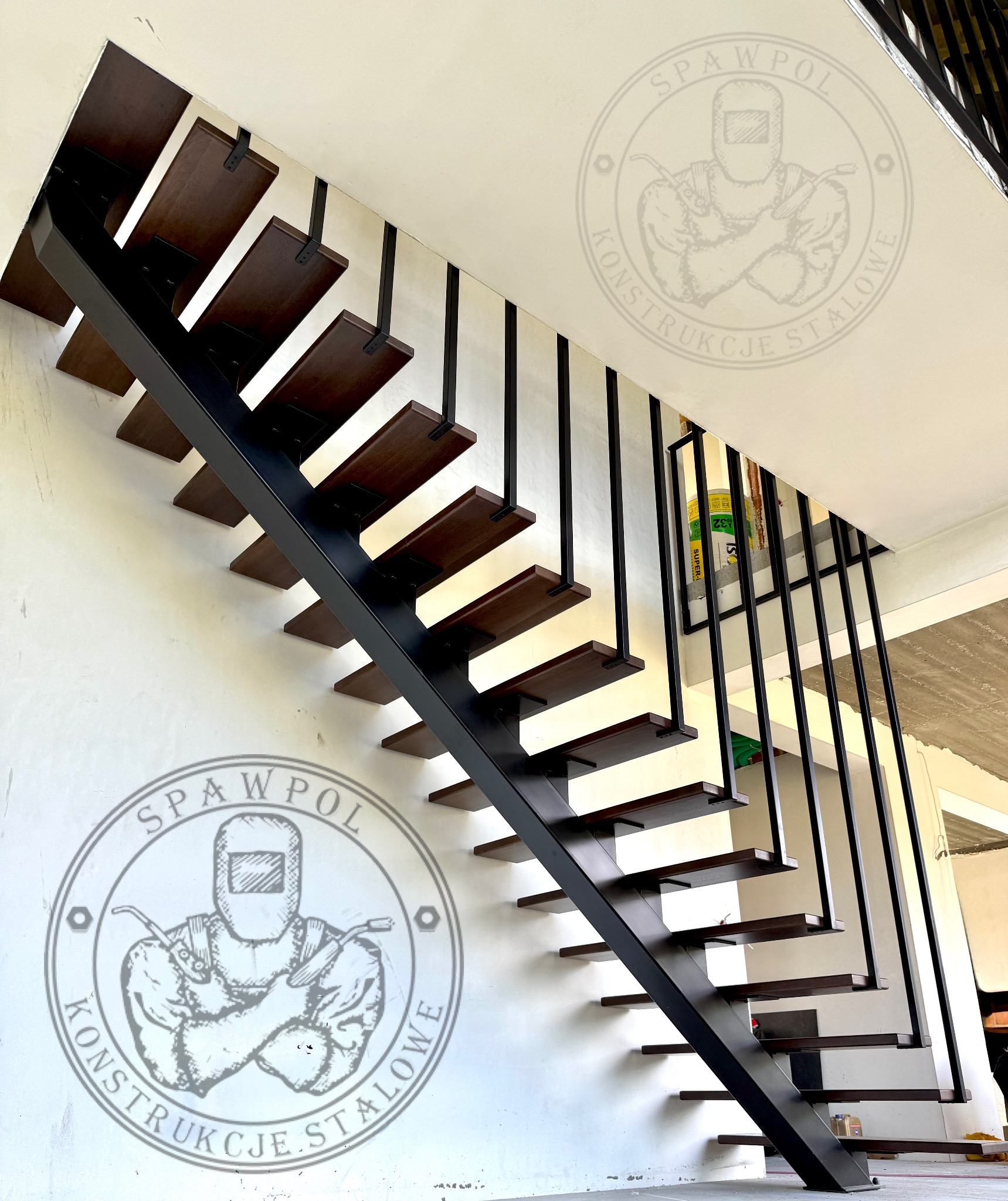 Nowoczesne schody z drewnianymi stopniami i czarną metalową konstrukcją, widok z dołu, z logo firmy na ścianie. Minimalistyczny design.