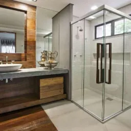 Nowoczesna łazienka z kabiną prysznicową ze szklanymi ścianami i drewnianymi uchwytami, umywalką na kamiennym blacie z drewnianą obudową oraz dużym lustrem w drewnianej ramie.