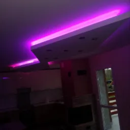 Nowoczesny salon z kuchnią, oświetlenie sufitowe LED w kolorze fioletowym, podwieszany sufit z punktowymi lampami, widok na kominek i wyjście na balkon.