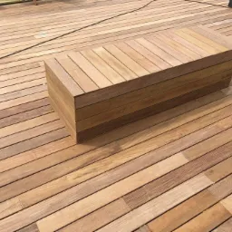 Świeżo ułożony drewniany taras z dopasowaną, geometryczną ławką z desek, wykończony w naturalnym odcieniu drewna.