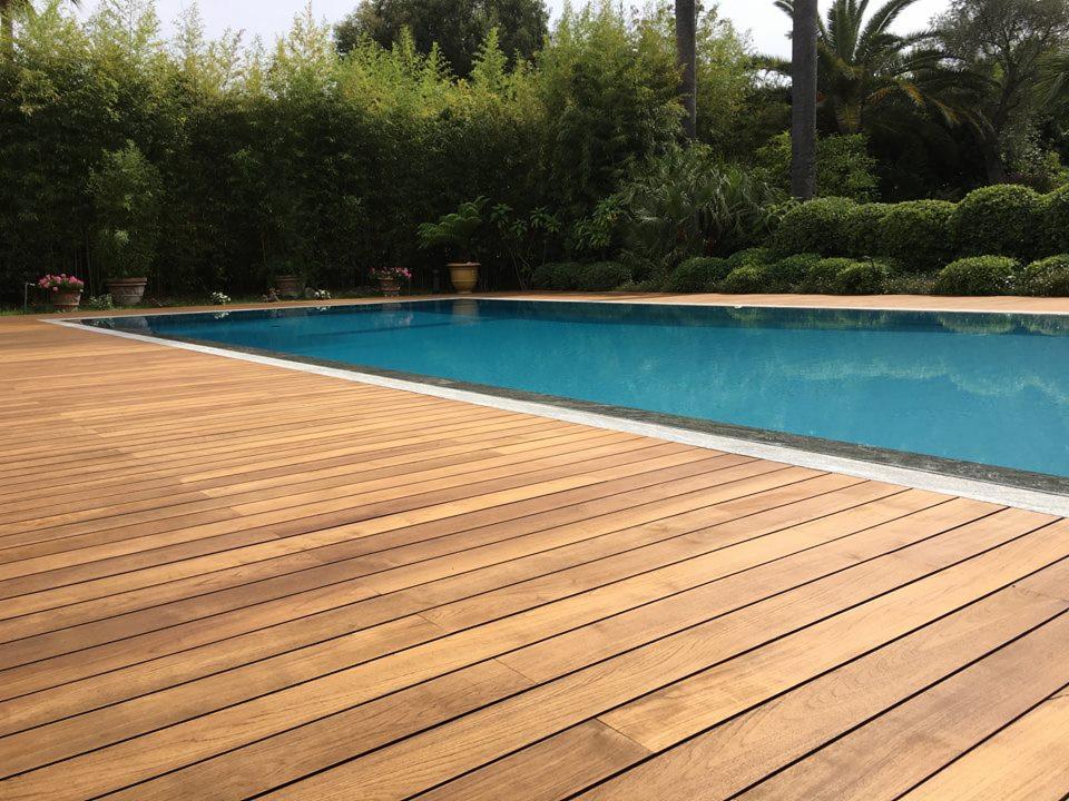 Nowoczesny taras z drewna egzotycznego wokół basenu, z roślinnością tropikalną w tle.